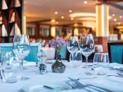 Elegant gedeckter Tisch im Restaurant der Douro Queen mit Gläsern, Besteck und Blumendeko. Im unscharfen Hintergrund das beleuchtete Schiffsrestaurant.