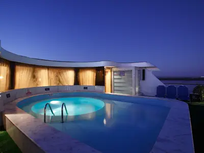 Das Sonnendeck der Jaz Nile Monarch am Abend: Ein beleuchteter Swimmingpool mit Jacuzzi, umgeben von Kabinenfenstern und Sitzgelegenheiten unter blauem Himmel.