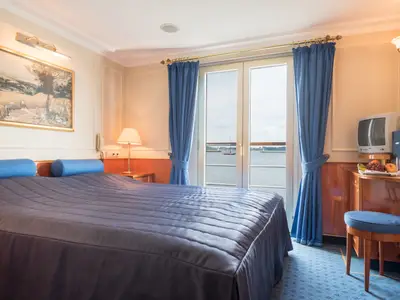 Kabine des Flusskreuzfahrtschiffs Katharina von Bora mit Bett, Balkontür zum Fluss, TV, Obst und Hocker. Klassisch eingerichtet.