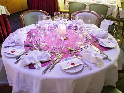 Ein festlich gedeckter Tisch im Speisesaal der La Belle de Cadix. Zu sehen sind Gläser, Besteck, Servietten, Menükarten und ein Teelicht.