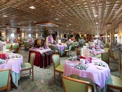 Das Restaurant der La Belle de Cadix zeigt gedeckte Tische mit rosa Decken und grünen Stühlen. Bullaugen und ein Weinfass schmücken das helle Schiffsambiente.