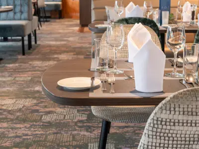 Gedeckter Tisch im Restaurant der Maxima mit Platzsets, Tellern, Besteck, Gläsern und weißen Servietten. Im Hintergrund sind weitere Tische der Schiffsgastronomie zu sehen.