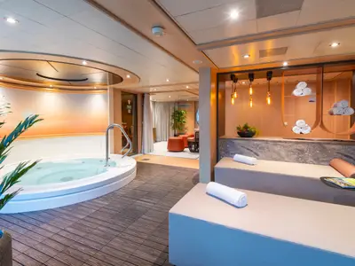 Wellnessbereich der Maxima: Großer Whirlpool, zwei Liegen mit Handtüchern. Moderne Einrichtung, warmes Licht und Holzboden. Angrenzend ein Loungebereich.