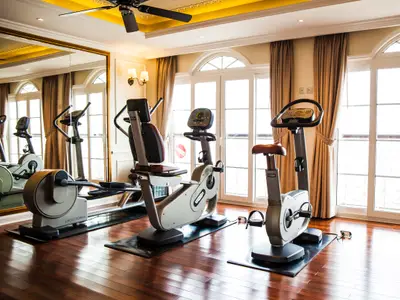 Innenansicht des Fitnessraums an Bord des Flusskreuzfahrtschiffs Mekong Navigator. Zu sehen sind mehrere Ergometer und ein Rudergerät, Spiegel und große Fenster mit Vorhängen.