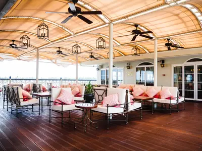 Offenes Deck des Mekong Navigator: Bequeme Sitzgruppen mit rosa Kissen unter einer Markise. Deckenventilatoren. Rechts die Schiffs-Lounge, links der Fluss.