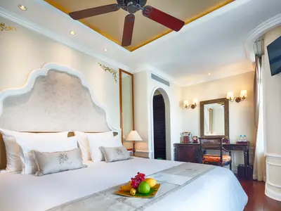 Geräumige Kabine der Mekong Navigator mit Doppelbett, weißer Bettwäsche, Obstteller, Deckenventilator und Schreibtisch mit Spiegel.
