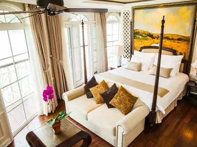 Innenansicht einer Kabine auf der Mekong Navigator. Man sieht ein großes Bett, ein Sofa, Nachttische mit Lampen, Fenster und ein Landschaftsgemälde.
