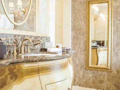 Luxuriöser Badezimmer-Waschtisch mit goldenen Armaturen und braunem Marmor. Gerolltes Handtuch, Badartikel und ein goldgerahmter Spiegel reflektieren den Raum.