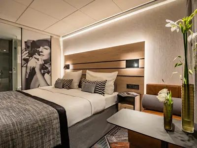 Moderne Kabine des Flusskreuzfahrtschiffs nickoSPIRIT mit Doppelbett, Holzkopfteil, Wandbild einer Fotografin und Beistelltisch mit Blumen.