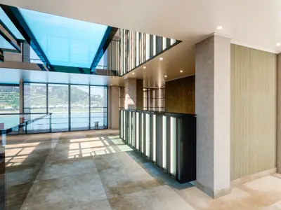 Der moderne Empfangsbereich der nickoSPIRIT mit Panoramafenstern bietet Blick auf eine Flusslandschaft. Eine beleuchtete Rezeption und eine Treppe mit Glaselementen kennzeichnen den hellen Innenraum.
