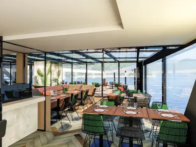 Helles Restaurant an Bord der nickoSPIRIT. Panoramafenster und Glasdach bieten weite Sicht auf Wasser und grüne Küste. Tische sind gedeckt, Stühle mit grünen Polstern.