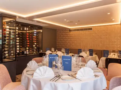 Ein stilvoll eingerichtetes Restaurant an Bord der nickoSPIRIT mit gedeckten Tischen und blauen Menükarten. Ein großer Weinkeller mit vielen Flaschen ist sichtbar, die Wände sind modern gestaltet.
