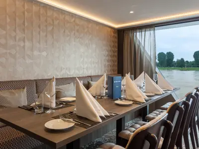 Blick in den Speisesaal der nickoSPIRIT mit gedeckten Tischen und Sitzen. Große Fenster erlauben Aussicht auf den Fluss mit Uferbäumen.