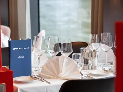 Ein gedeckter Tisch auf dem Flusskreuzfahrtschiff nickoSPIRIT. Er zeigt Gläser, Besteck, Servietten, Salz- und Pfefferstreuer und eine Menükarte, bereit für die Gäste.