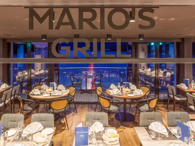 Das Restaurant Mario's Grill auf der nickoSPIRIT zeigt gedeckte Tische und moderne Möbel. Durch große Fenster ist die blaue Nacht zu sehen.