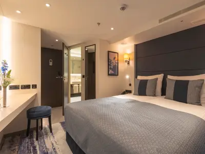 Moderne Doppelkabine der nickoVISION mit Bett, blauen Akzenten, Schreibtisch und Badzugang. Warme Beleuchtung.