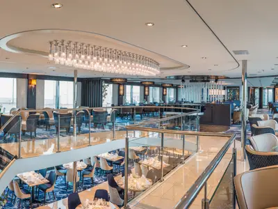 Restaurant der nickoVISION auf zwei Ebenen. Tische, Stühle, blaue Teppiche, Panoramafenster, Hängeleuchte und geschwungene Treppe.