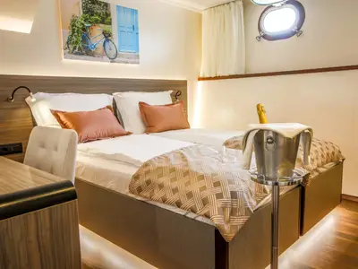 Helle Kabine des Flusskreuzfahrtschiffs Princess. Zwei Betten, Schreibtisch, Bullauge, Champagnerkühler. Moderne Einrichtung der Princess mit Holz- und Weißtönen.