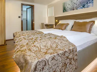 Moderne Kabine auf der Princess. Zwei Betten mit braun-goldener Tagesdecke, Holzboden und ein Schrank sind sichtbar. Über dem Bett hängt ein Bild mit Tautropfen.