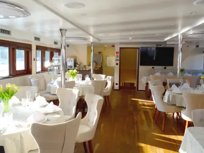 Blick ins helle Restaurant des Flusskreuzfahrtschiffs Princess. Elegant gedeckte Tische, helle Stühle, große Fenster und Holzboden. Sonnenlicht fällt ein.