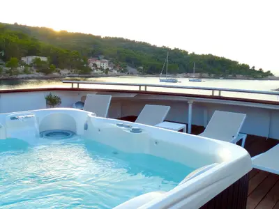 Whirlpool und Sonnenliegen auf dem Deck der Princess. Im Hintergrund liegt eine Bucht mit grünen Hügeln, Häusern und Segelbooten bei Sonnenuntergang.
