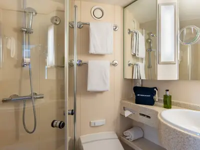 Modernes, helles Badezimmer an Bord der Rhein Melodie von nicko cruises. Zu sehen sind eine Duschkabine, Waschbecken, Toilette, Spiegel, frische Handtücher und Pflegeprodukte.