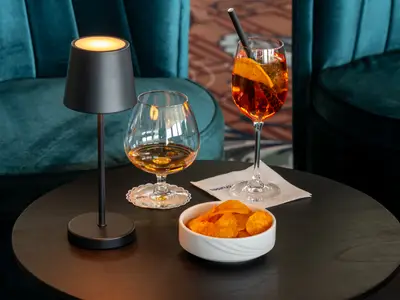 Tisch in der Bar der Rhein Melodie mit Lampe, Brandy, Aperol Spritz und Chips. Im Hintergrund türkisfarbene Sessel des Flusskreuzfahrtschiffs Rhein Melodie.
