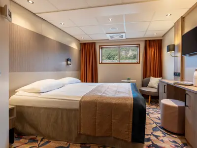 Innenansicht einer Kabine auf dem Flusskreuzfahrtschiff Rhein Symphonie. Zu sehen sind ein Bett, Schreibtisch mit TV und ein Fenster mit Blick auf eine Burg am Fluss.