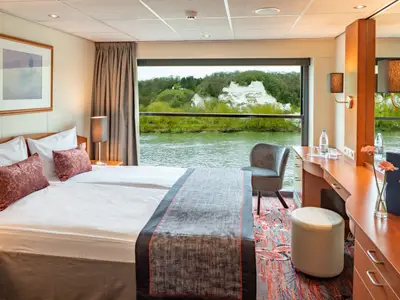 Eine geräumige Kabine an Bord der Seine Comtesse mit einem Doppelbett, großem Panoramafenster und Blick auf den Fluss. Rechts ein Schminktisch.
