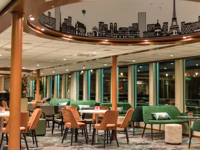 Blick in die gemütliche Lounge der Seine Comtesse mit grünen Sofas und orangen Stühlen. Große Fensterfront und Deckenverzierung mit Pariser Skyline, inklusive Eiffelturm und Arc de Triomphe.