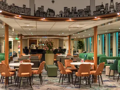 Die Lounge der Seine Comtesse mit orangefarbenen Stühlen und grünen Sofas. Eine Bar und eine Stadtsilhouette an der Decke sind zu sehen.