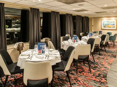 Blick in den Speisesaal der Seine Comtesse mit runden, weiß gedeckten Tischen, modernen Stühlen, großen Fenstern und einem bunten Teppichboden.