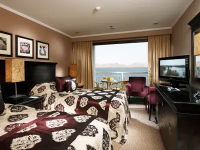 Kabine auf dem Flusskreuzfahrtschiff Steigenberger Omar El Khayam. Man sieht zwei Betten, einen Fernseher, dunkle Möbel und einen Balkon mit Blick auf Fluss und Landschaft.