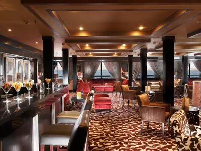 Bar- und Loungebereich Steigenberger Omar El Khayam. Theke mit Früchten, Barhocker, rote Sofas, braune Sessel, gemusterter Teppich, Fenster, Flussblick.
