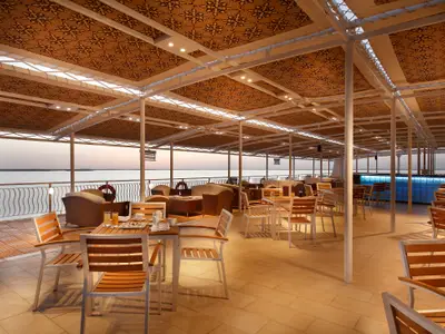 Das Sonnendeck der Steigenberger Omar El Khayam zeigt Tische, Stühle, Lounge-Möbel und eine beleuchtete Bar. Im Hintergrund ist ein Fluss bei Sonnenuntergang.