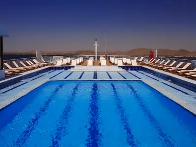 Deckansicht des Flusskreuzfahrtschiffs Steigenberger Omar El Khayam: Großer Pool, viele Sonnenliegen, Mast. Dahinter erstrecken sich Wasser und karge Berge.