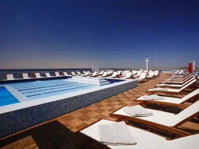 Sonnendeck des Steigenberger Omar El Khayam mit Pool, weißen Sonnenliegen und Handtüchern. Dahinter Wasser, karge Uferlandschaft unter blauem Himmel.