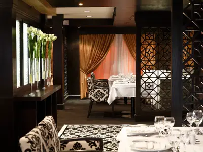 Das Restaurant auf dem Flusskreuzfahrtschiff Steigenberger Omar El Khayam zeigt gedeckte Tische, dunkle Holzelemente und goldene Vorhänge für ein elegantes Ambiente.