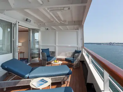 Balkon des Flusskreuzfahrtschiffs Vasco da Gama. Blaue Liegen, Sessel, Tische auf Holzdecking. Meerblick mit Industrieanlagen.