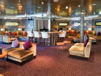 Lounge des Flusskreuzfahrtschiffs Vasco da Gama: Bar mit Hockern, Sofas, Sessel, bunte Kissen und kleine Tische. Ein Klavierbereich ist hinten sichtbar.