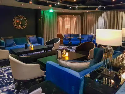 Einblick in den eleganten Lounge-Bereich des Kreuzfahrtschiffs Vasco da Gama. Man sieht blaue Sofas, Sessel, dunkle Tische mit Dekoration und eine stimmungsvolle Beleuchtung.