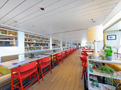 Das helle Restaurant des Flusskreuzfahrtschiffs Vasco da Gama. Es zeigt rote Stühle, lange Tische, dekorative Regale und große Fenster. Ein moderner und einladender Speisesaal.