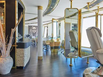 Friseursalon auf der Vasco da Gama: Goldene Spiegel, helle Stühle, dunkler Holzboden und eine Empfangstheke mit Steinmosaik.