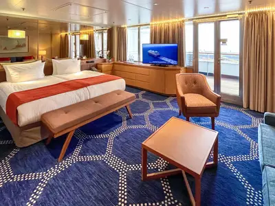 Innenansicht einer luxuriösen Kabine auf dem Flusskreuzfahrtschiff Vasco da Gama mit Doppelbett, Sitzbereich, TV und Zugang zum eigenen Balkon. Blauer Teppich mit Muster.