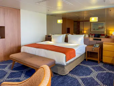 Kabine des Kreuzfahrtschiffs Vasco da Gama: Großes Doppelbett, orange Decke, blauer Teppich mit Muster und Spiegelwand, die einen Wohnbereich zeigt.