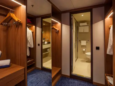 Einblick in eine moderne Kabine der Vasco da Gama mit offenem Schrank, großem Spiegel und Badezimmer mit WC. Handtücher liegen bereit.
