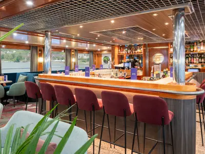 Bar-Lounge der Viktoria mit langer Theke, roten Hockern und gefüllten Regalen. Gemütliche Sitzbereiche und Fenster mit Flusslandschaftsblick.