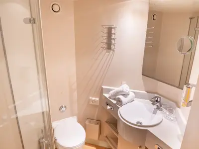 Dieses Bild zeigt ein kleines, helles Badezimmer an Bord des Flusskreuzfahrtschiffs Viktoria. Es umfasst eine Duschkabine, ein WC, ein Waschbecken mit Handtüchern und einen Spiegel.