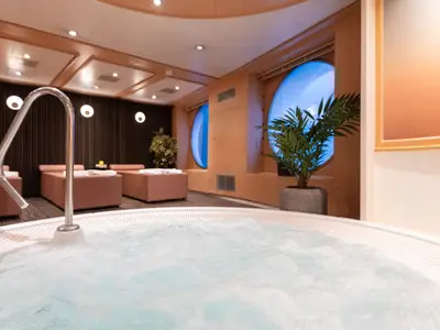 Detailansicht eines sprudelnden Whirlpools an Bord der nicko cruises Viktoria. Im Hintergrund sind komfortable Liegen, Pflanzen und runde Fenster zu sehen.