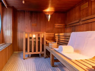 Blick in die holzgetäfelte Sauna an Bord der Viktoria. Der Raum hat Holzbänke, einen Ofen, ein Handtuchset, einen Saunakübel und ein großes rundes Fenster.